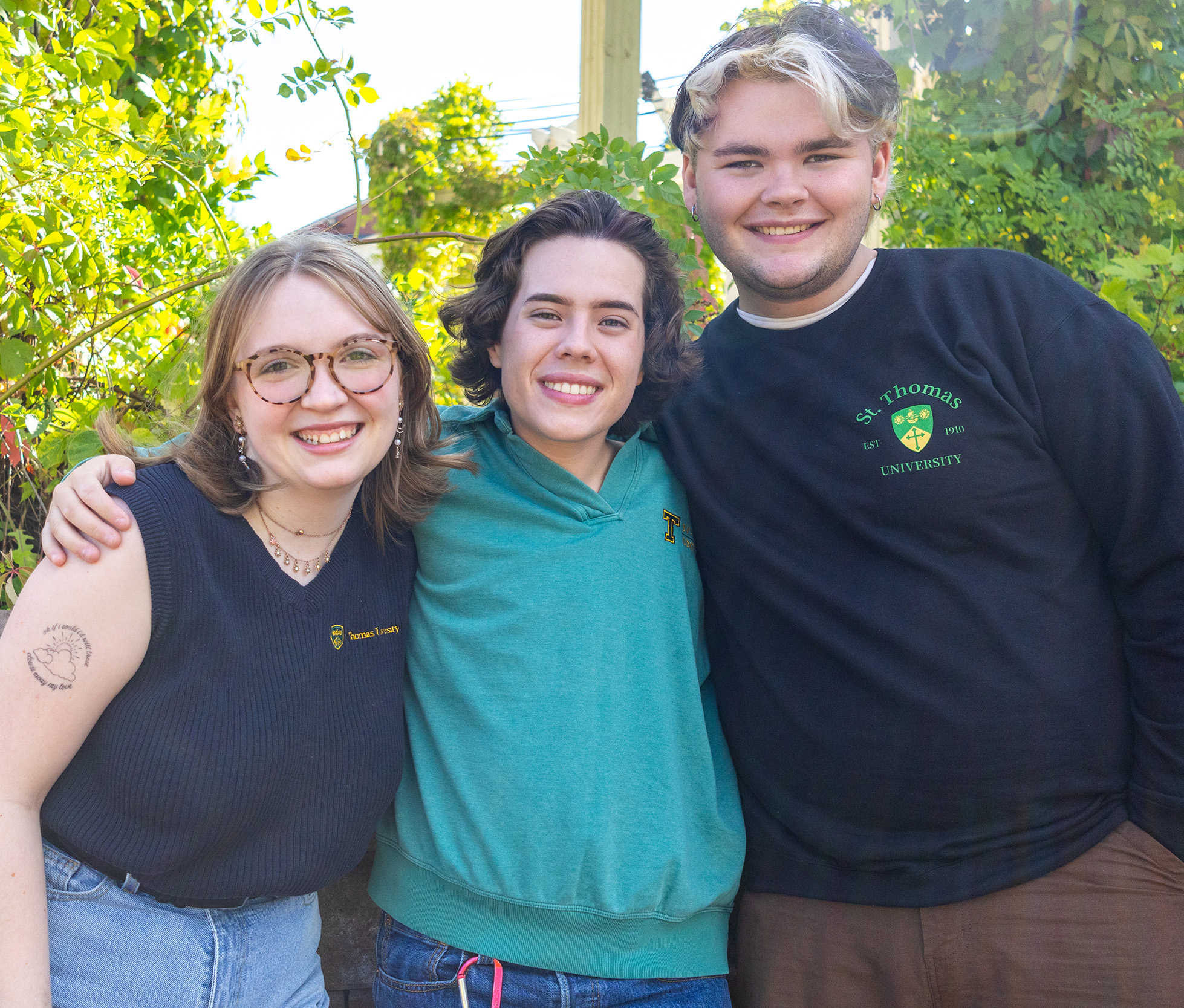 Three students stand arm in arm on campus