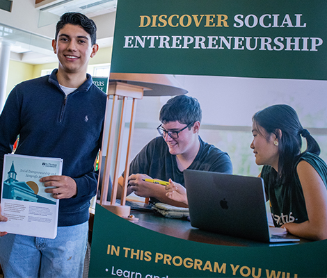 Male student holding program sheet next to Social Entrepreneurship Banner at Open House