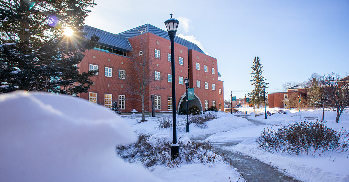 Picture of snowy campus and sun peeking through trees