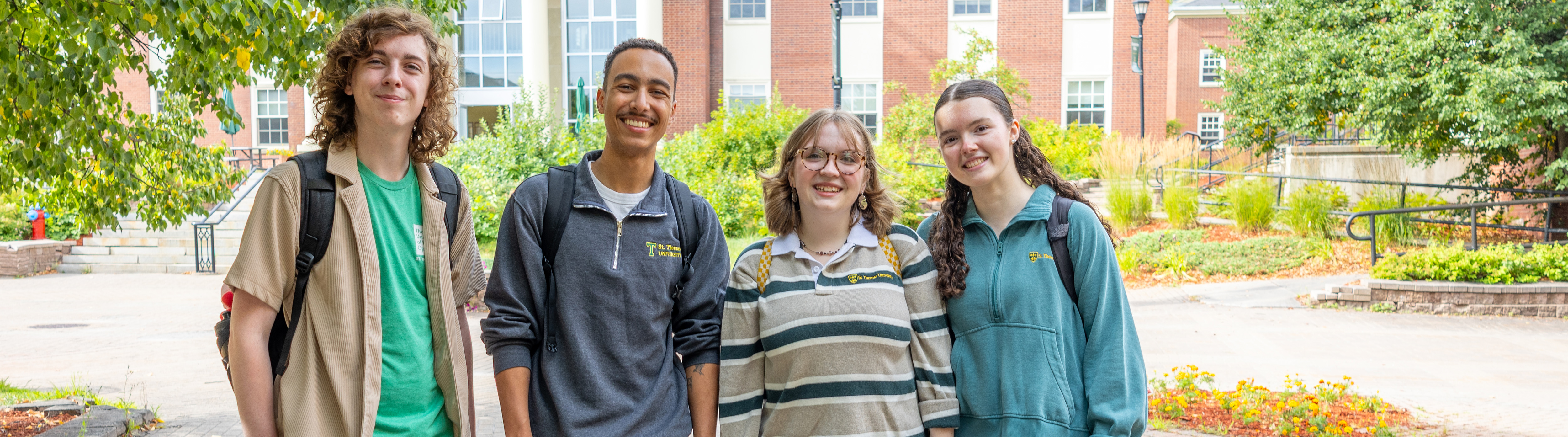A group of students - two male and two female - stand outside on campus