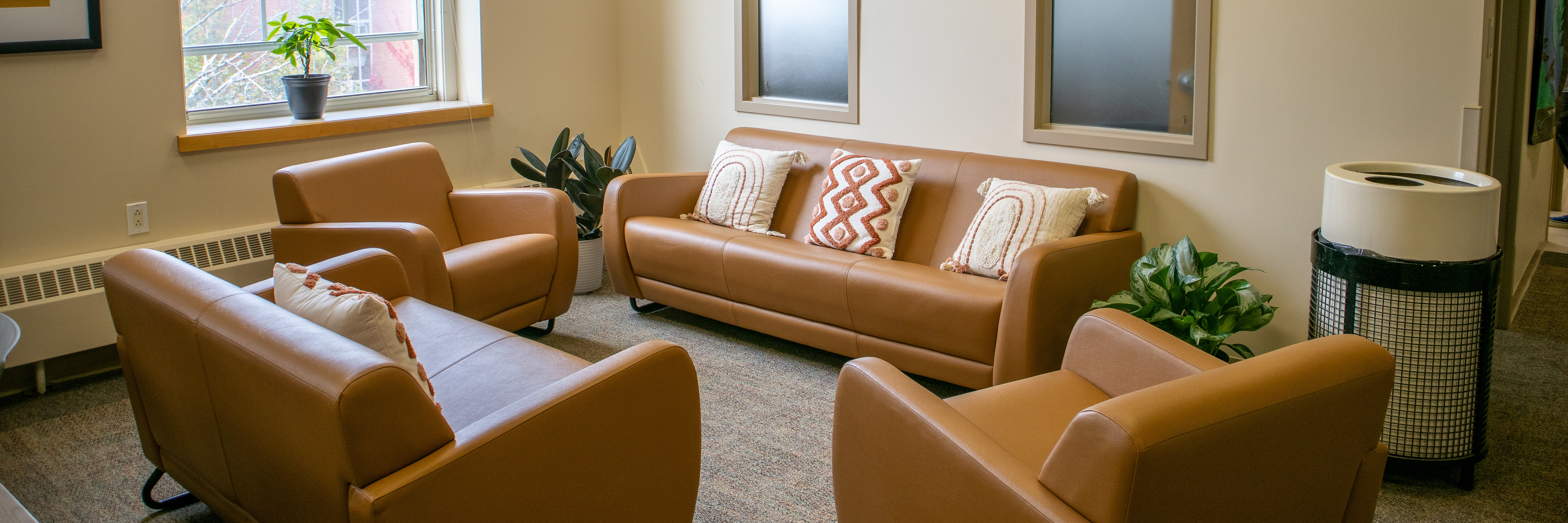 Four burnt orange couches with decorative pillows arranged in a circle on top of a gray carpet.