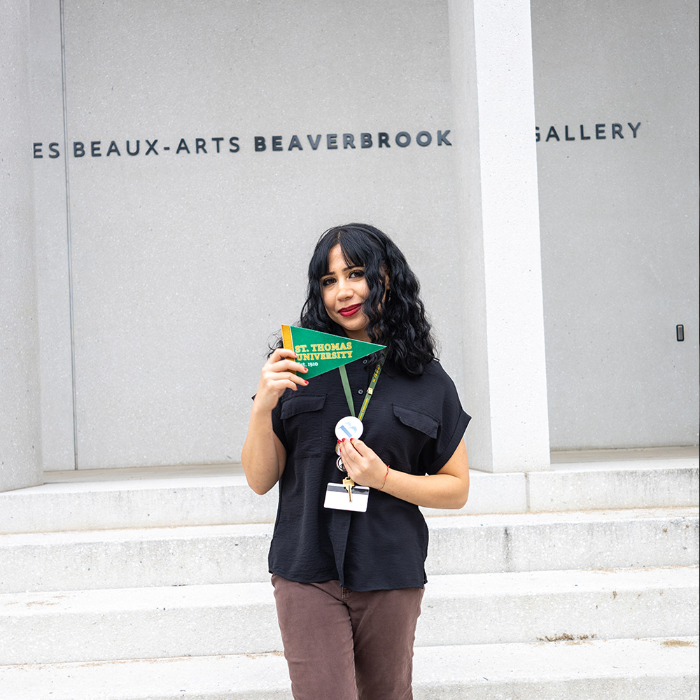A female student stands on the steps outside of the Beaverbrook Art Gallery, holding out a STU pennant