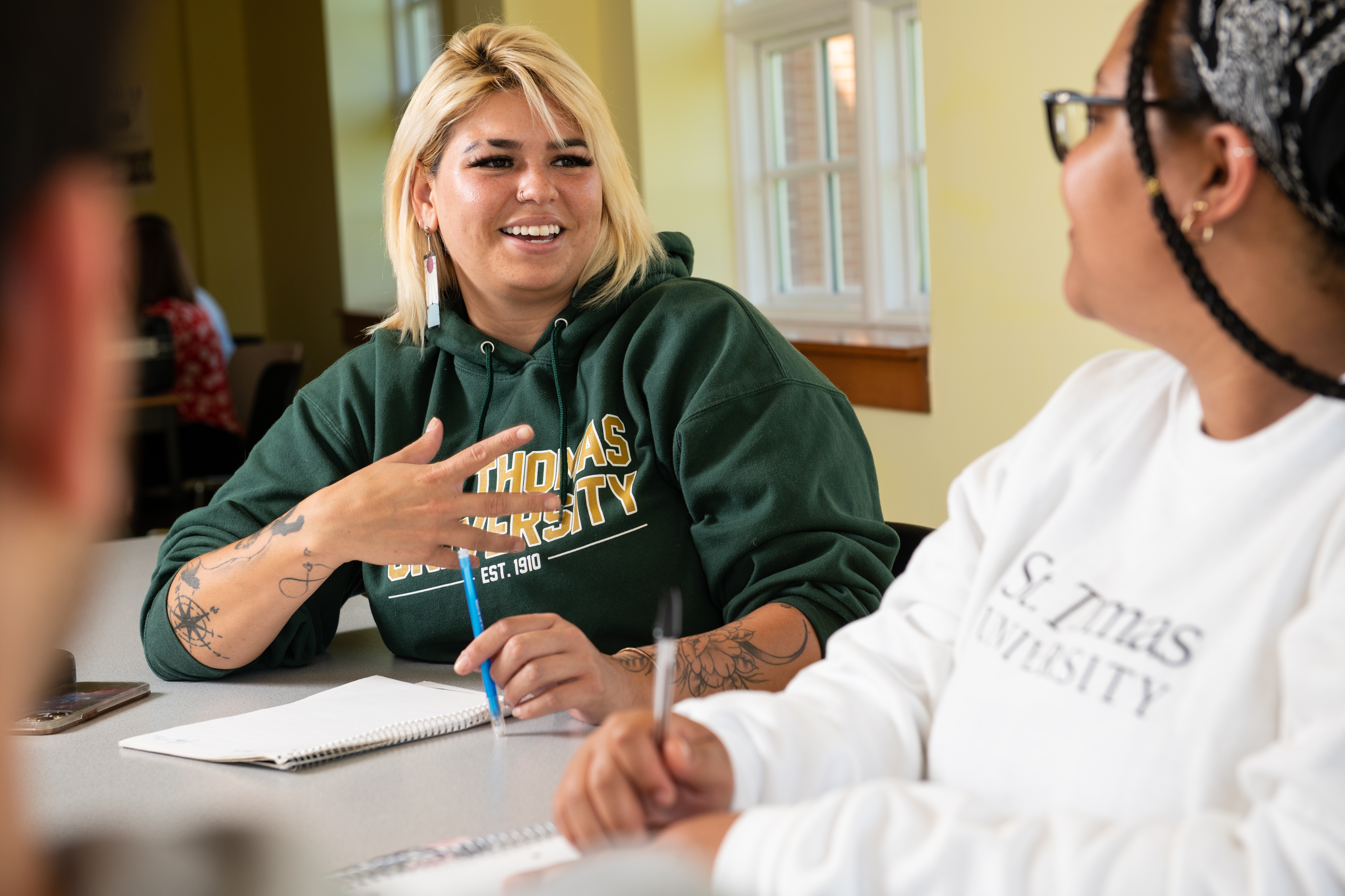 Two students wearing STU hoodies talking in a classroom