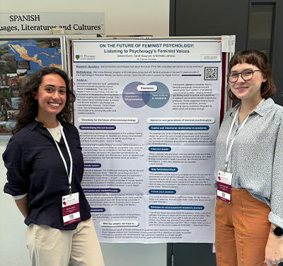Two female STUdents smiling and standing next to poster at an academic conference