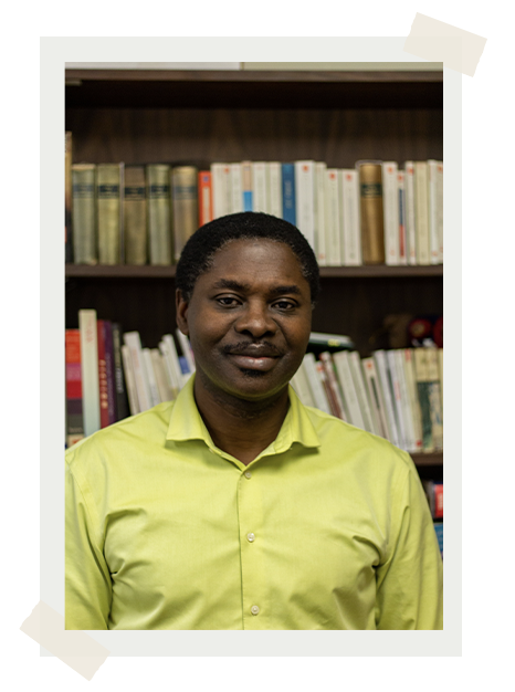 Portrait of Dr. Christian Mbarga, standing in front of a bookshelf