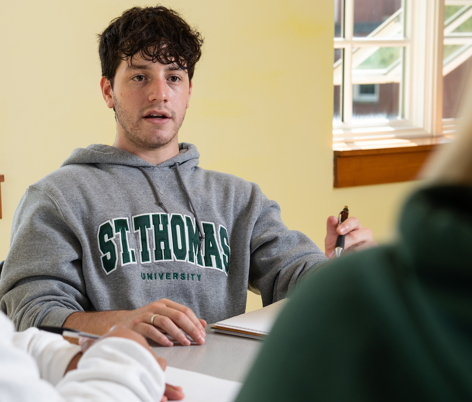 photo of a male student with a STU hoodie on in class, talking