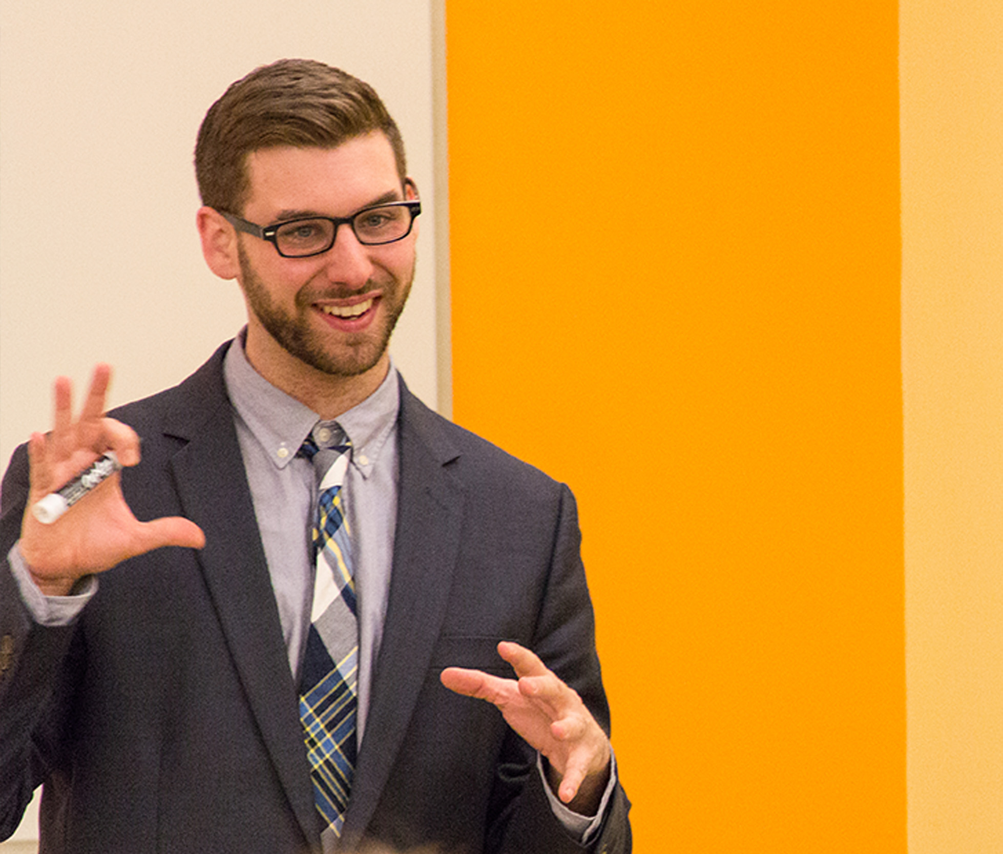 A photo of a great books professor teaching in a classroom, wearing a suit and classroom is yello