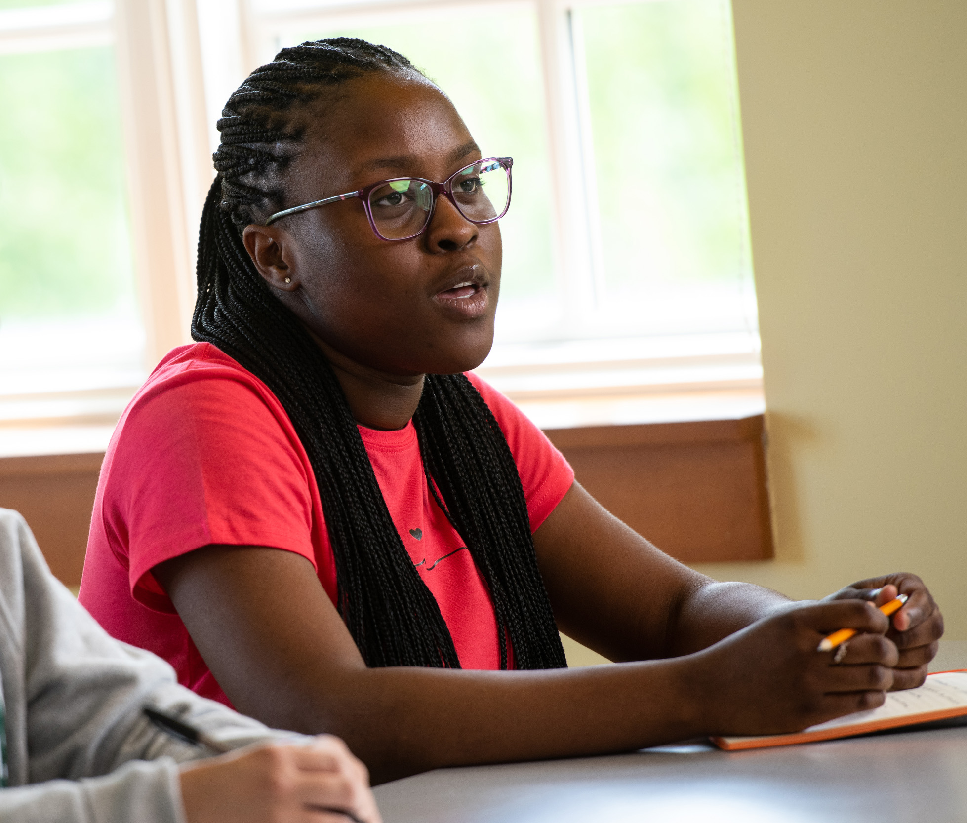 A photo of a student sitting in class, talking, wearing a bright pink shirt