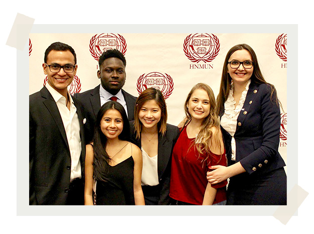Six students stand in front of a Model UN backdrop at the Model UN in Boston