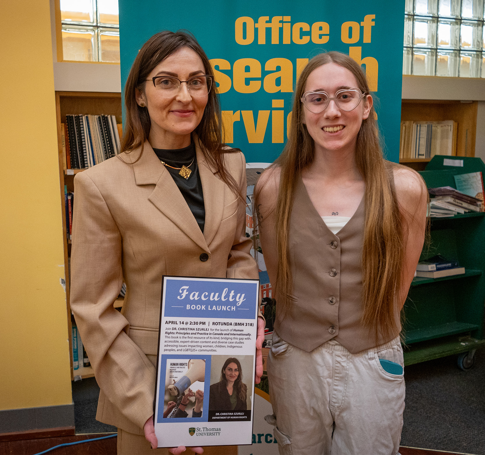 Professor Christina Szurlej stands with a student holding up a plaque commemorating the launch of her new book.